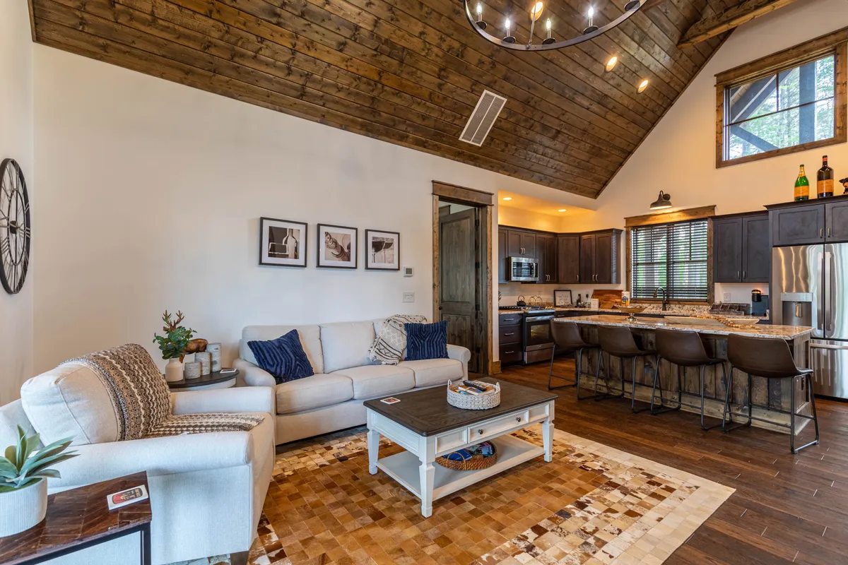 An inviting interior living space featuring a comfortable sofa, a modern kitchen island, a wooden ceiling, and decorative artwork. The design blends comfort and function, hinting at plush linens, fresh towels, and the overall cozy ambiance.