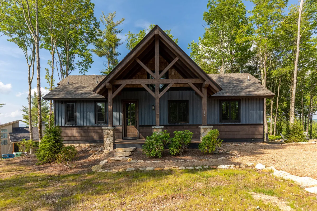 The image showcases the inviting exterior of a single-family house with an A-frame roof, sturdy stone foundation, manicured landscaping, and a welcoming front entrance. The porch overlooks scenic mountain views, perfect for enjoying sunsets, while the outdoor space hints at cozy gatherings and evenings spent around a fire pit.