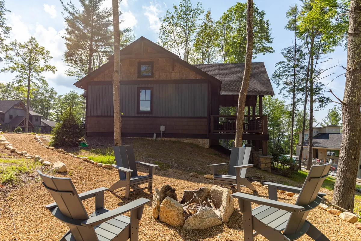 An inviting fire pit surrounded by comfortable seating, set against a backdrop of wooded surroundings and the main house. The area is prepared for cozy evenings of conversation or s’mores under the stars.