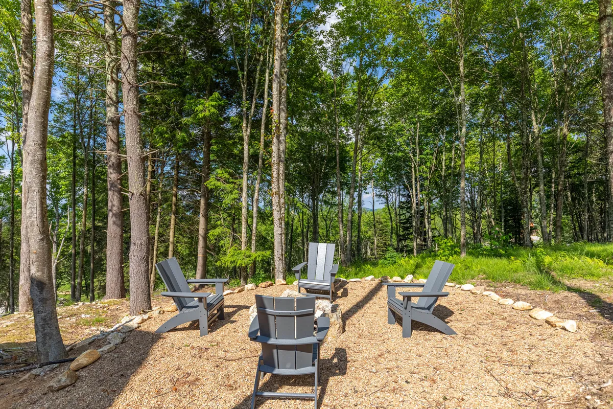 A cozy outdoor seating area with Adirondack chairs encircles a fire pit amid towering trees. The backdrop of the forest creates a tranquil environment, evoking the perfect spot for relaxation after a day of adventure.