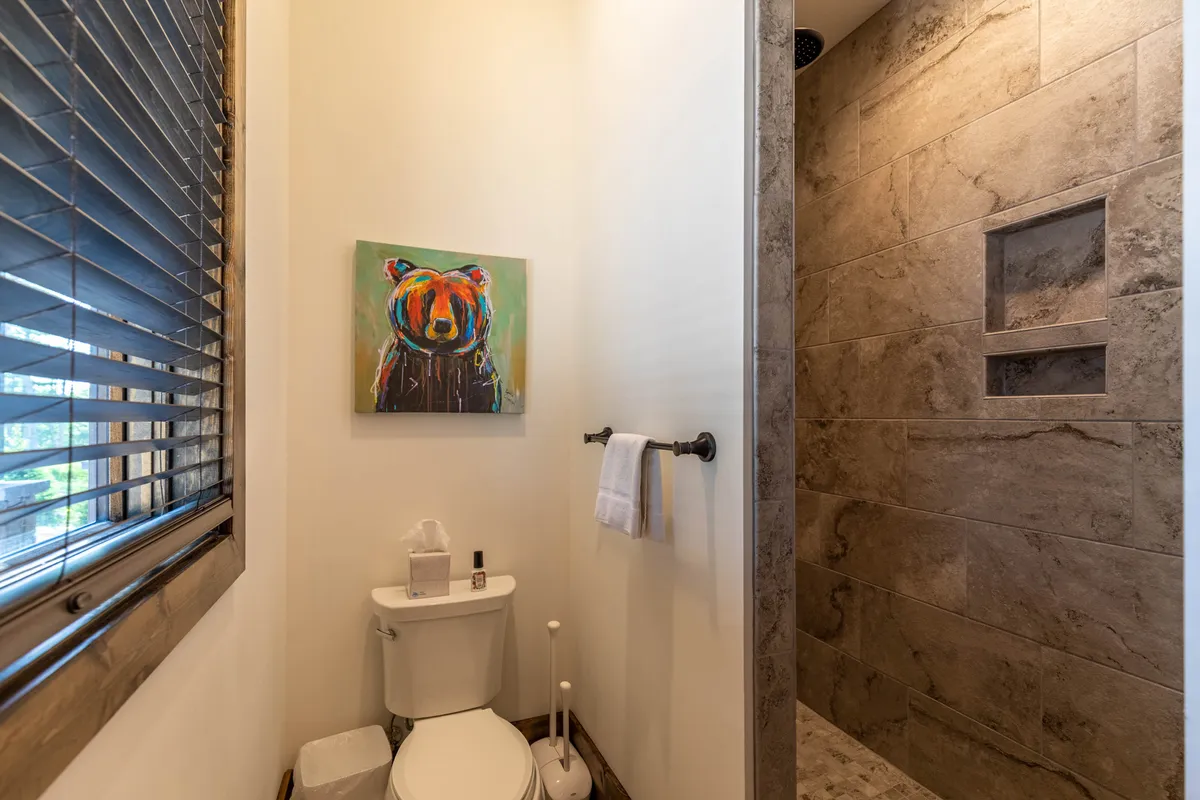 A modern powder room featuring a colorful bear painting, contemporary toilet, and textured shower wall. The playful yet cozy design adds a memorable, convenient touch to the guest experience.