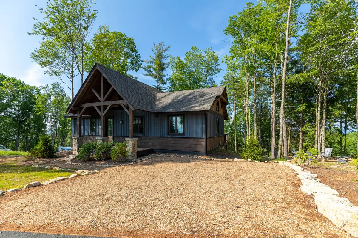 A welcoming mountain home surrounded by lush greenery, with a gravel driveway leading up to the entrance. The scene is serene, inviting, and emphasizes the privacy and tranquility of a mountain retreat.